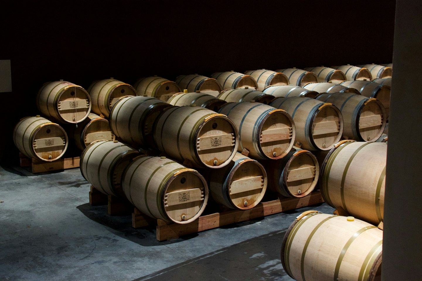 Stacked wooden wine barrels rest on a concrete cellar floor.